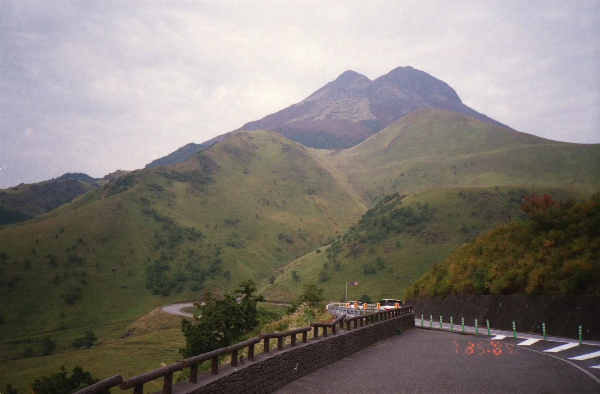Green mountain with twin peaks above a winding road and guardrail